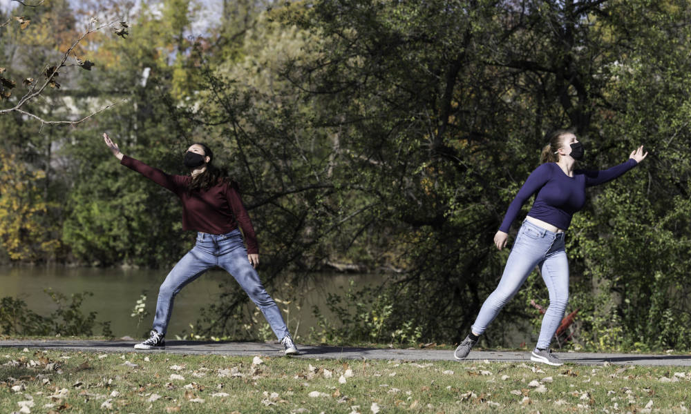 Two students dance on the sidewalk along the Genesee River.