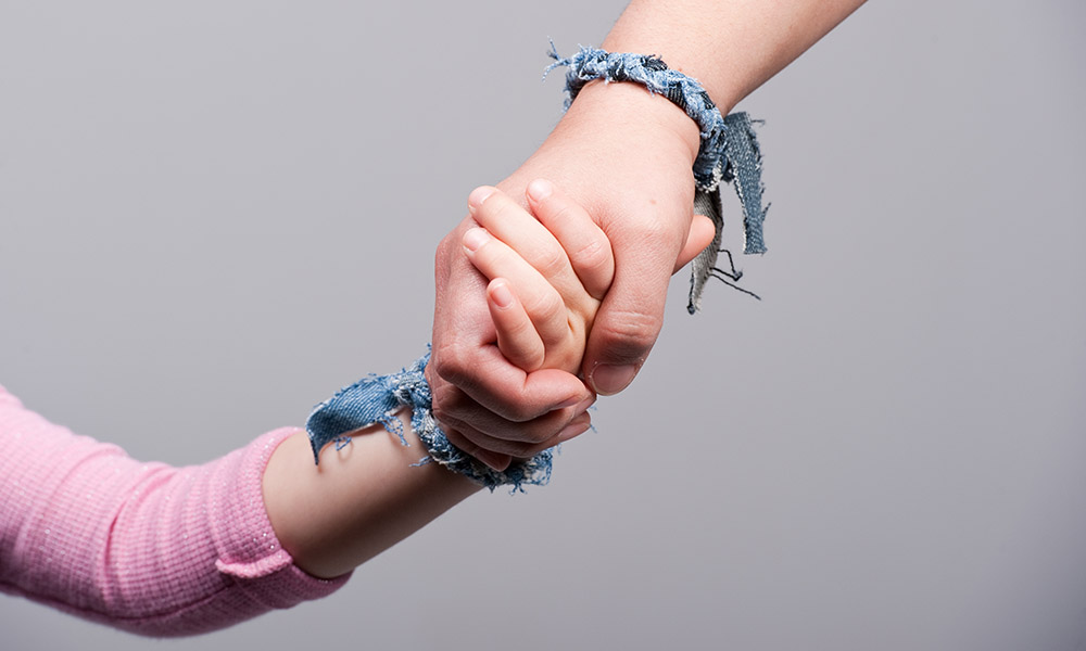 Hands of a child and a young adult clasped together.