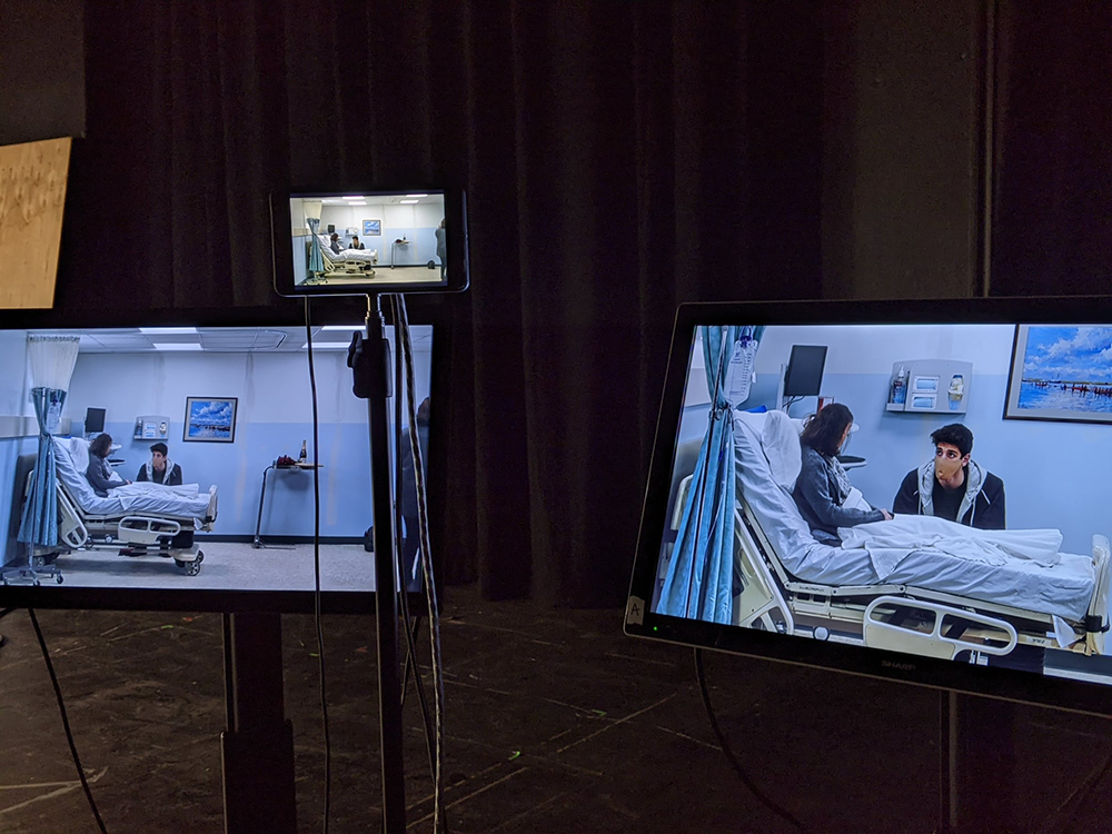 Three computer screens, two large and one small, showing the same hospital bed scene with two actors.