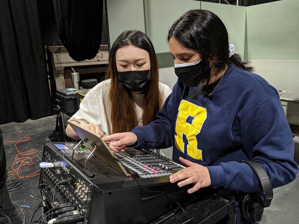 two students in COVID masks working over a large sound board.