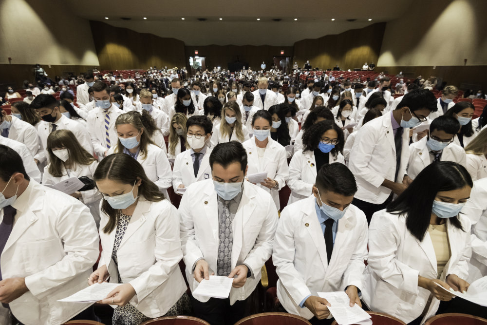Wide angle shot of students donning their white coats and masks while reciting their code of conduct in unison. 
