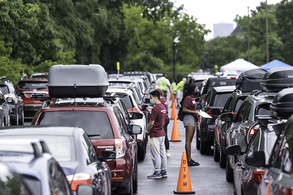 students stand among rows of cars in a parking lot