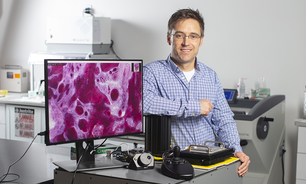 Giacomelli stands next to imaging system featuring large screen image of biopsied skin tissue.