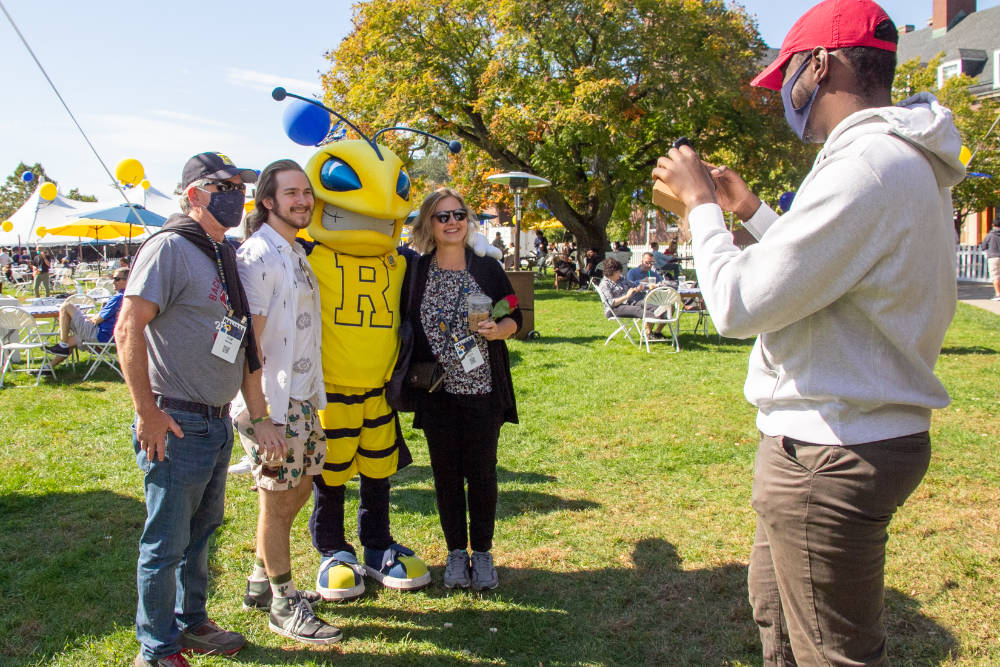 Three people with Yellowjacket mascot Rocky pose while someone takes a photo of them during Meliora 2021.