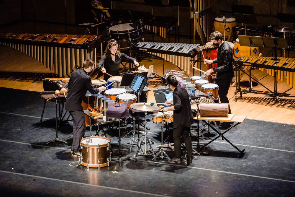 Four members of the Eastman Percussion Ensemble play instruments together on stage.