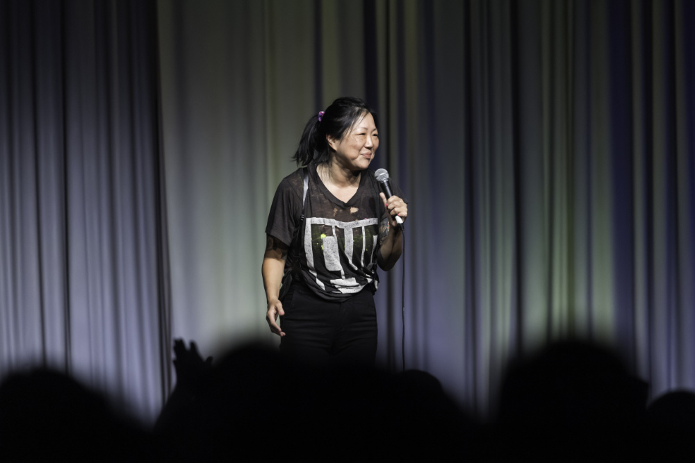 Margaret Cho smiles and holds a microphone on stage.