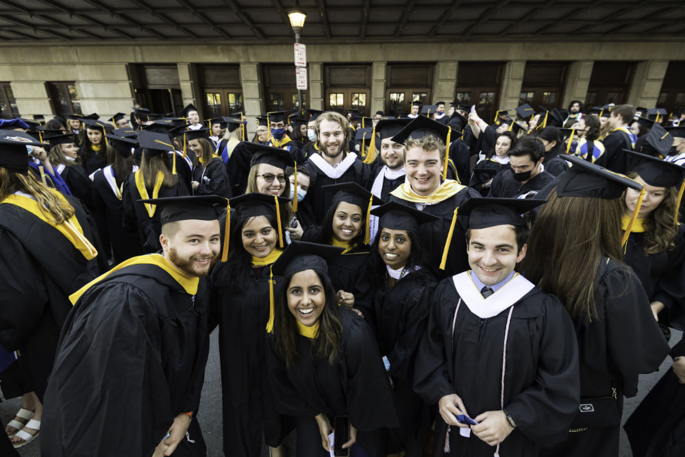 Several students garbed in regalia huddle together to smile for a group photo during Meliora 2021's commencement ceremony.