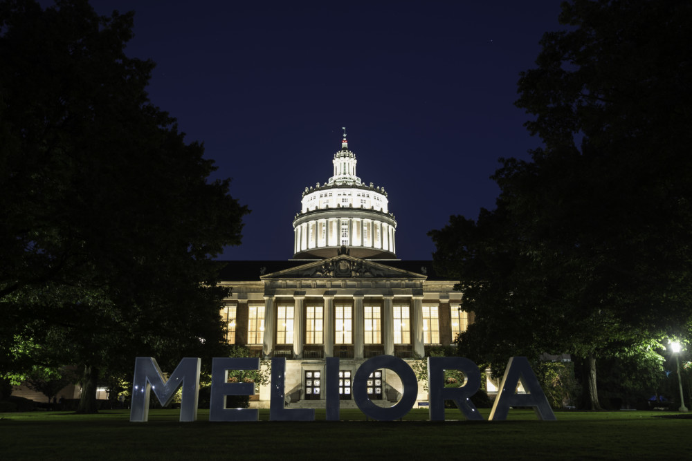 Meliora letters lit up from behind by Rush Rhees Library at twilight.