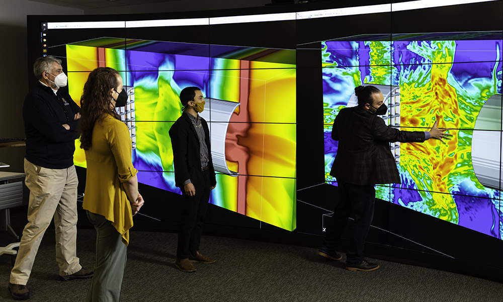 Researchers looking on at wall-sized, vividly colored screens showing simulations of laser-driven experiments.