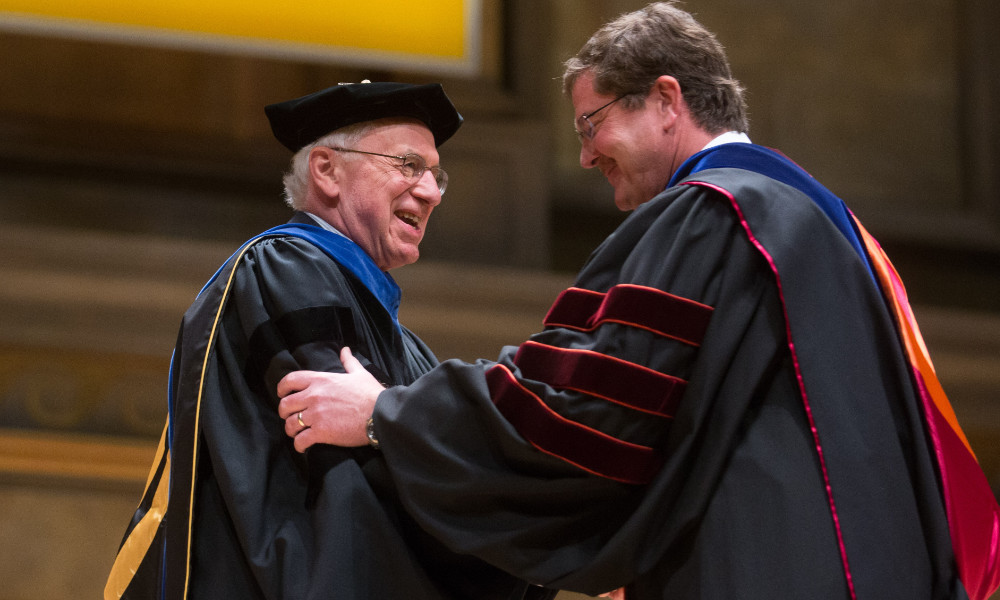 Clad in commencement robes, John Thomas shakes hands with Rob Clark at the Hajim School's diploma ceremony.