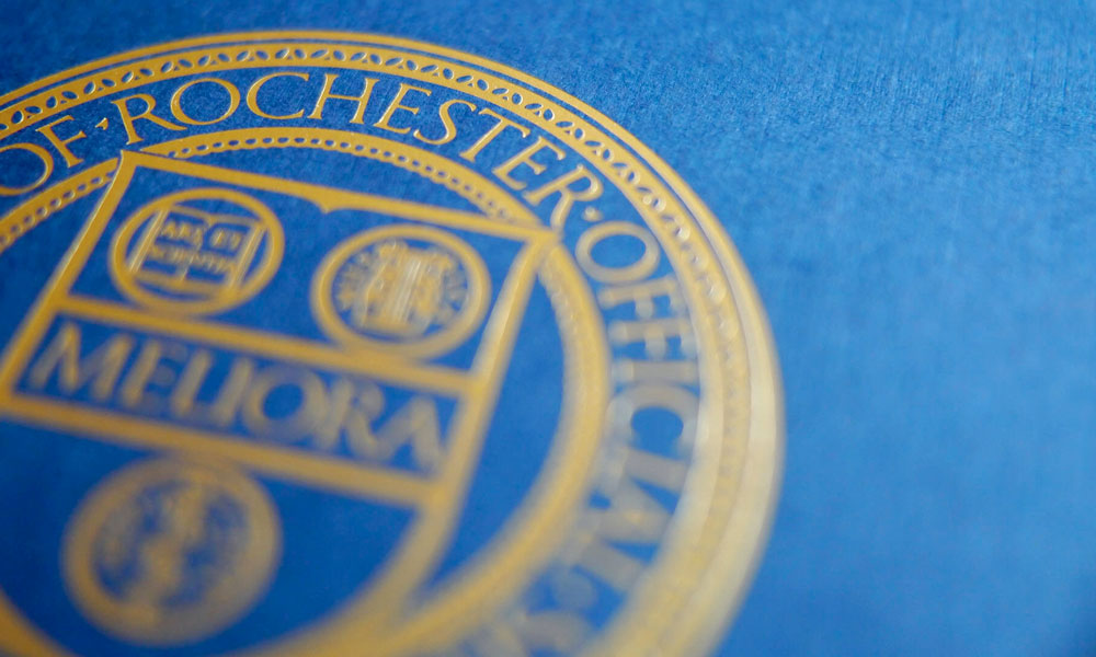 Closeup of the University of Rochester seal rendered in gold against a blue background.