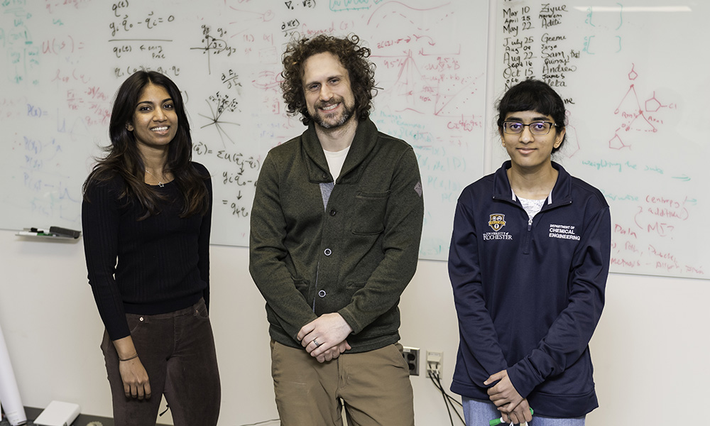 three researchers standing in front of a board filled with equations