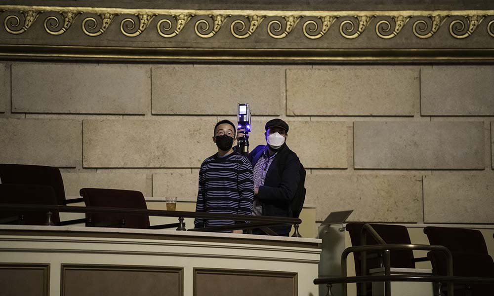 Two men stand on balcony with laser scanner.