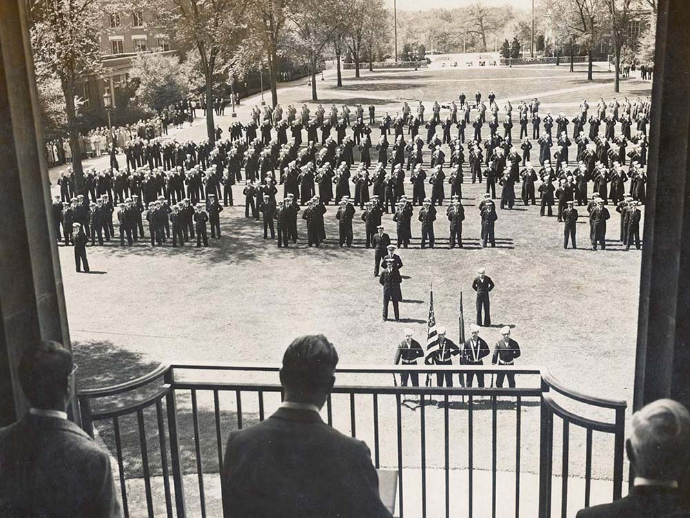 President Valentine shown from behind addressing Navy trainees on campus quad.