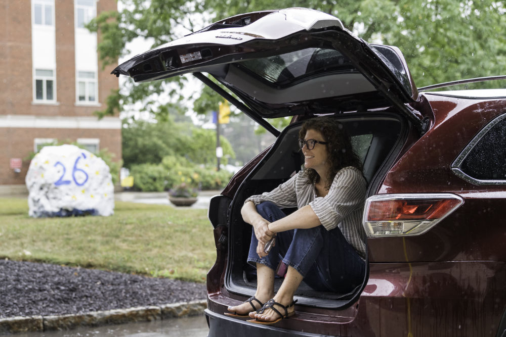 College student's mom sits in the open trunk of a car while it pours rain outside.