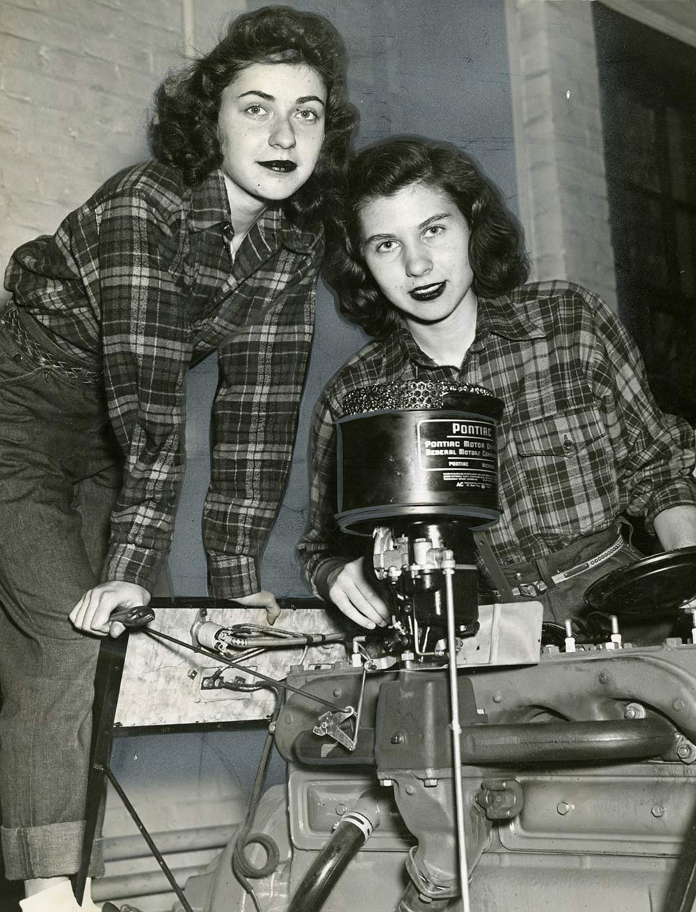 Two women students in plaid shirts work on motor.