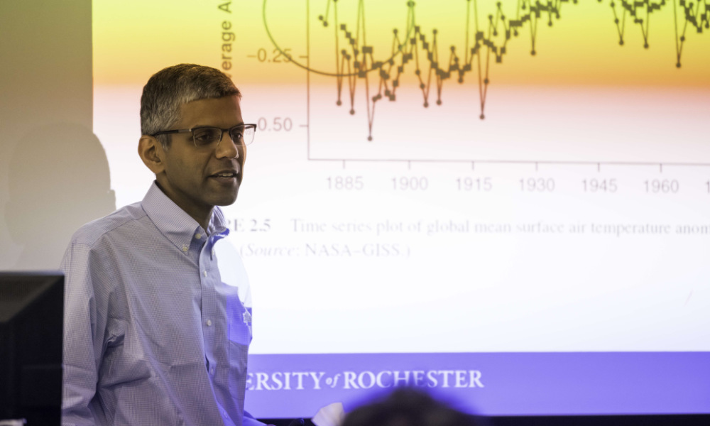 Ajay Anand lecturing in front of a PowerPoint screen.