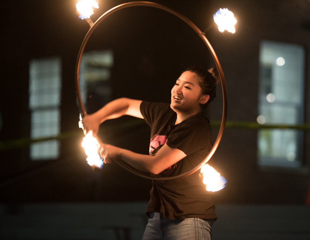 Woman juggles hula hoop with four flames attached to it.
