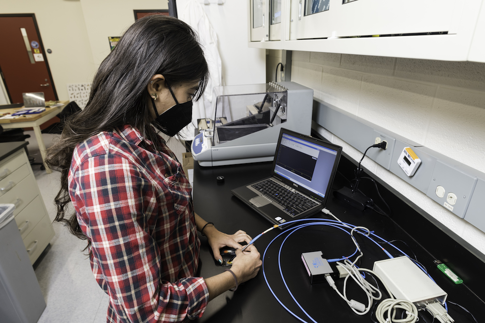 Maria Castano holds a long wire over a feather sample.