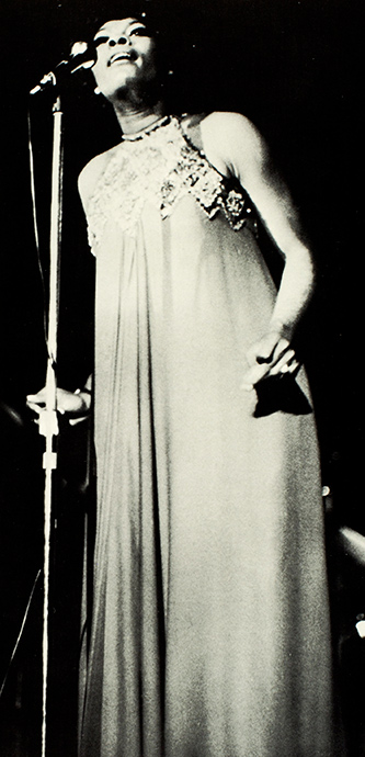 archival concert photo of Dionne Warwick singing at the microphone.