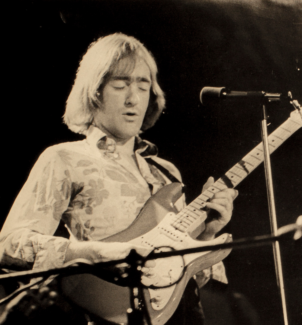 archival concert photo of Dave Mason playing the guitar.