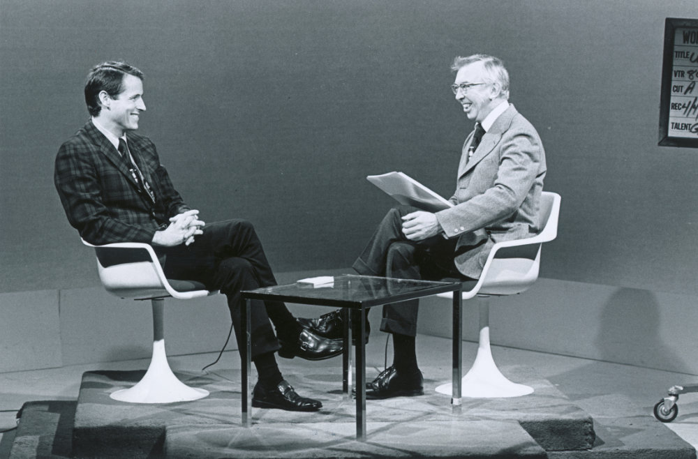 Black-and-white archival photo of a TV set with host Don Lyon and his guest seated and conversing. 