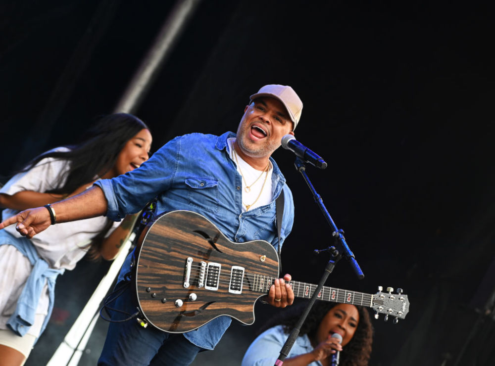 Gospel music singer Israel Houghton plays a guitar and performs two background vocalists on stage at the 2021 ESENCE Festival of Culture.