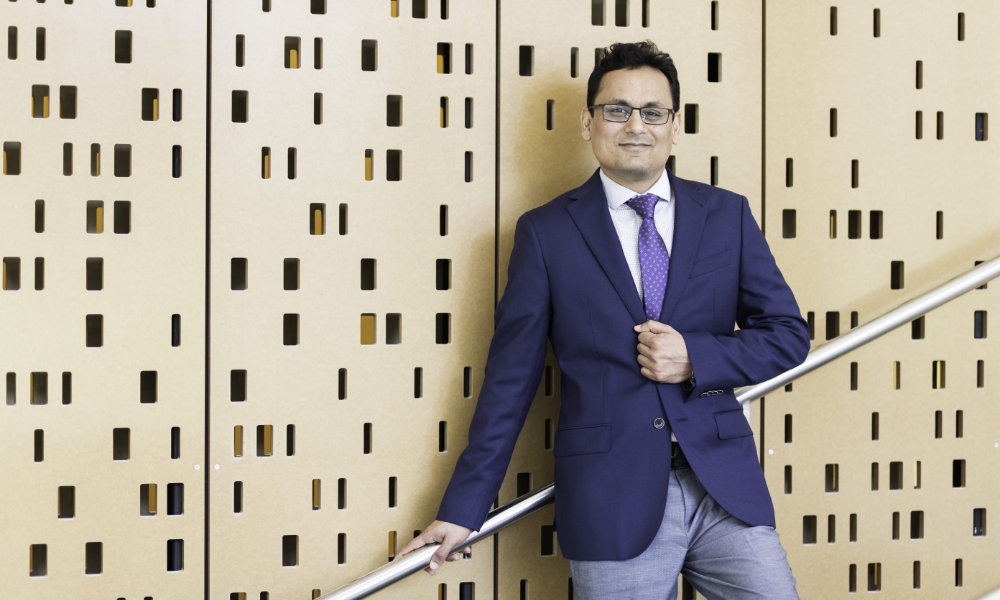 Ehsan Hoque poses on a stairwell against a wall that looks like a punchcard.