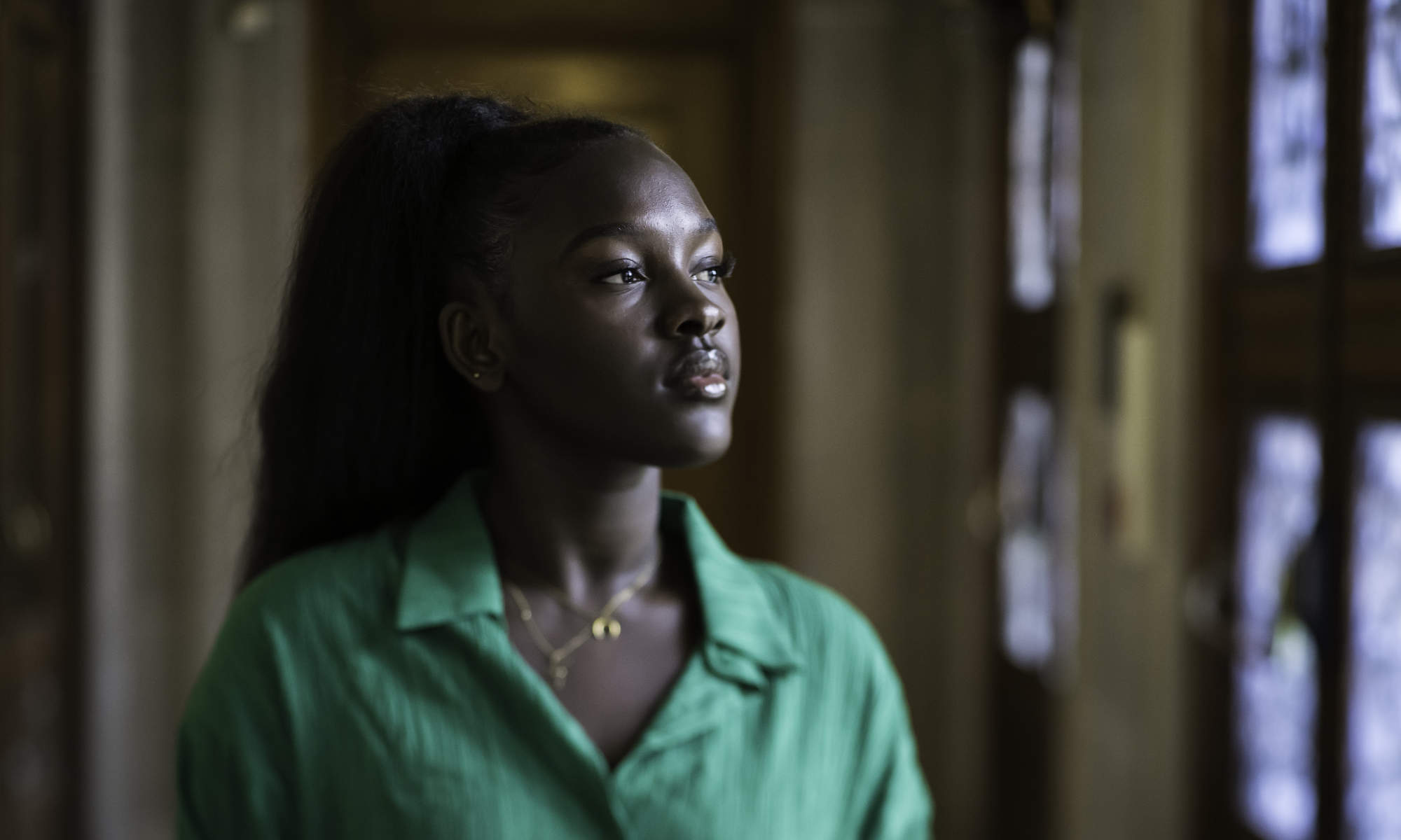 Fatou Jobe wearing bright green while looking off camera in a library entryway.