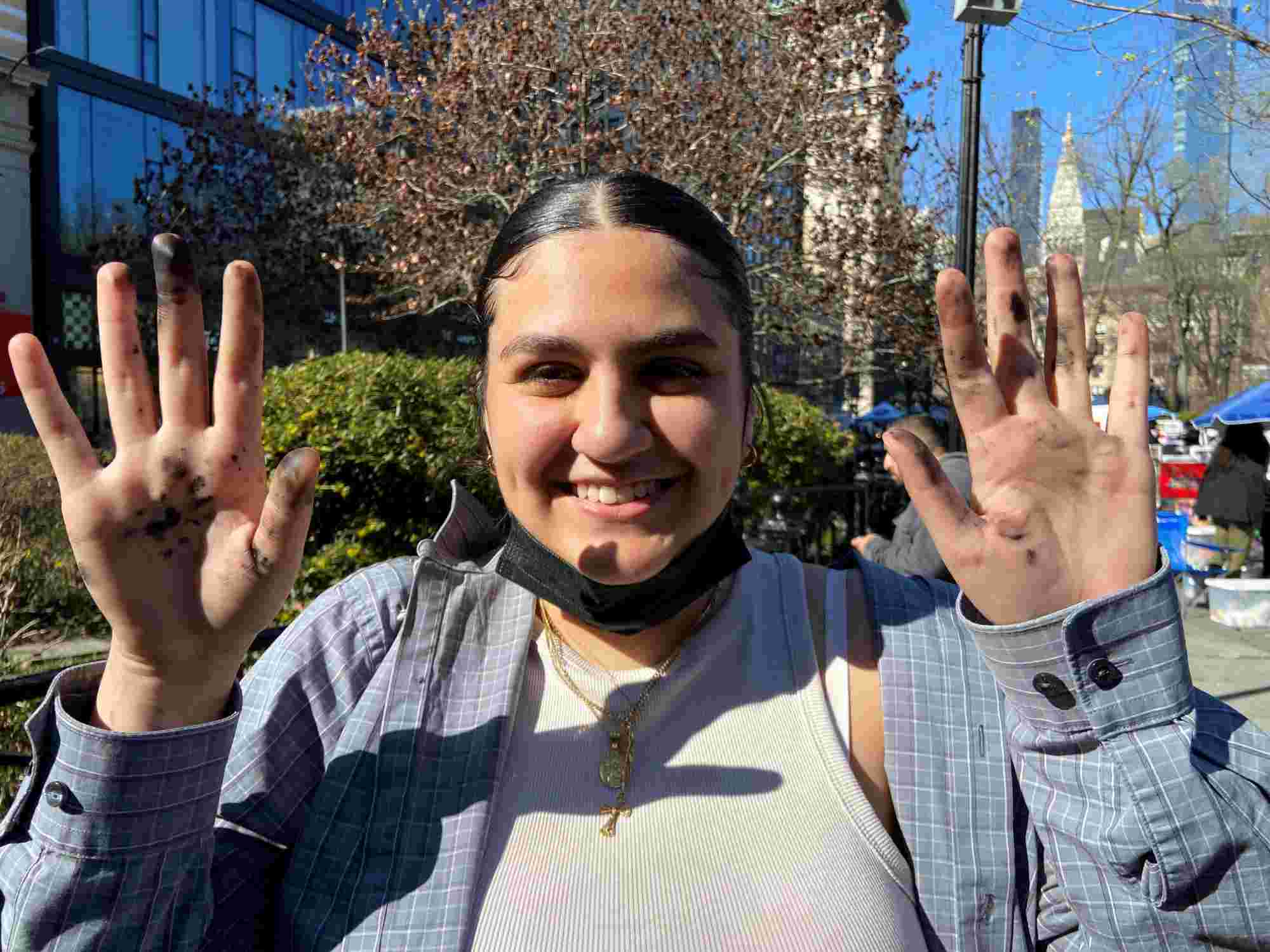 Art New York student Angelica Aranda holds up two hands stained with ink while smiling in New York City.