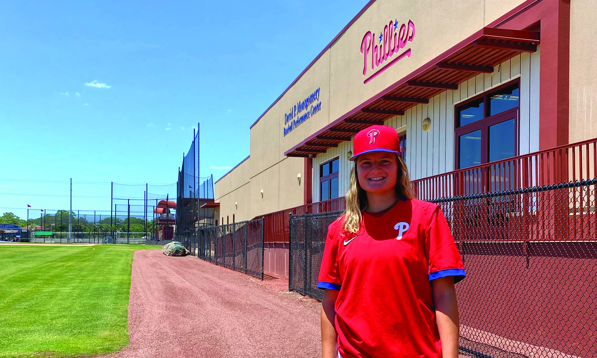 Beth Greenwood, wearing a Philadelphia Phillies hat and T-shirt stands beside a team training center.