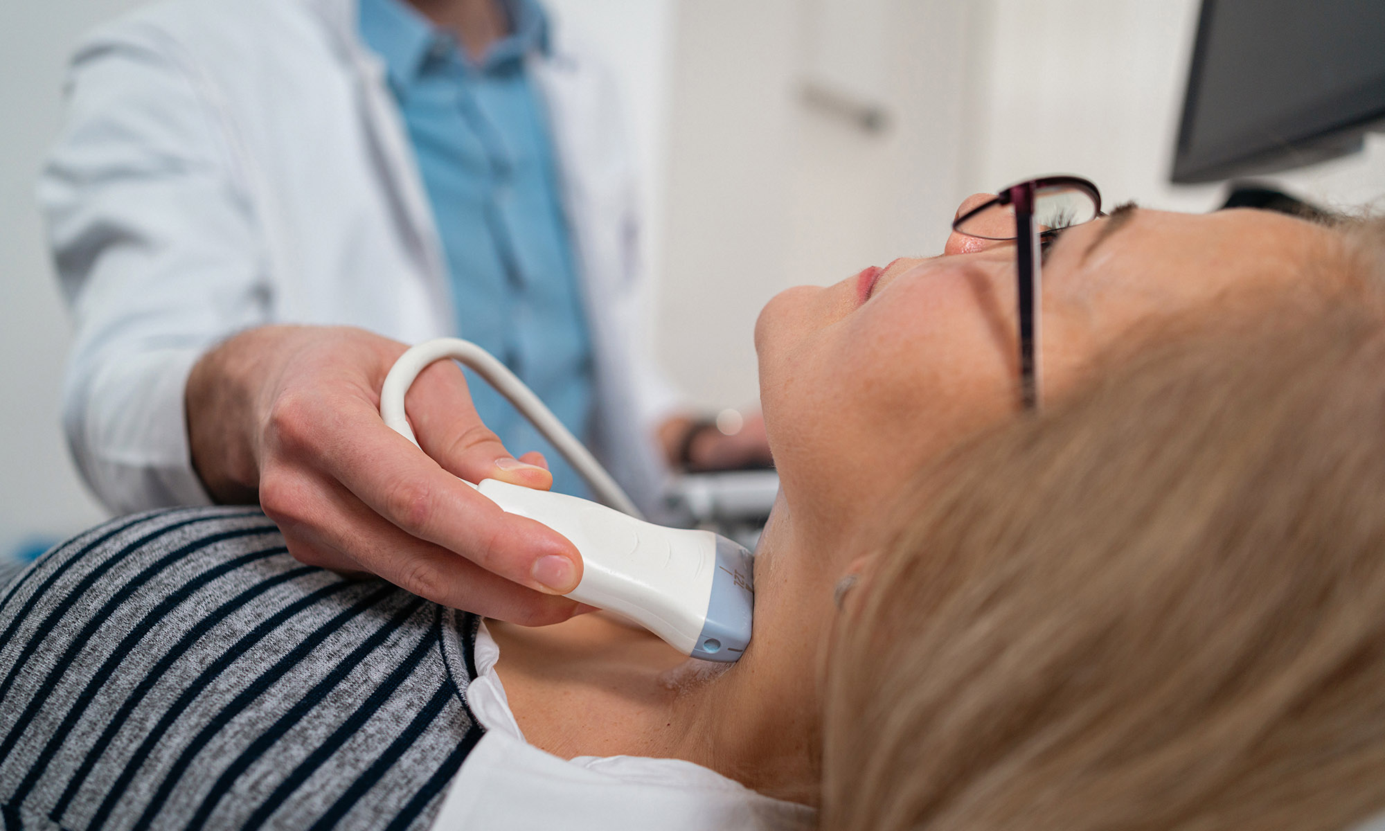 medical provider holds ultrasound wand to woman's neck.