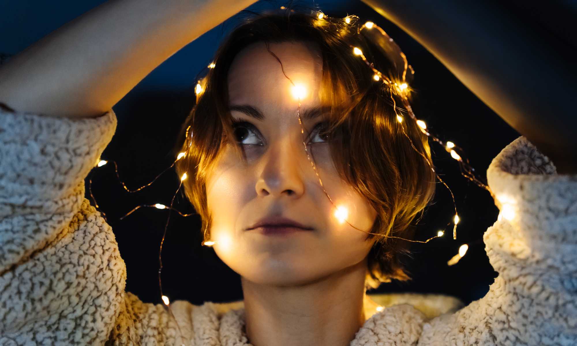 Woman with a string of lit lights around her head and arms raised during the nighttime to illustrate the concept of bioluminescent optogenetics.