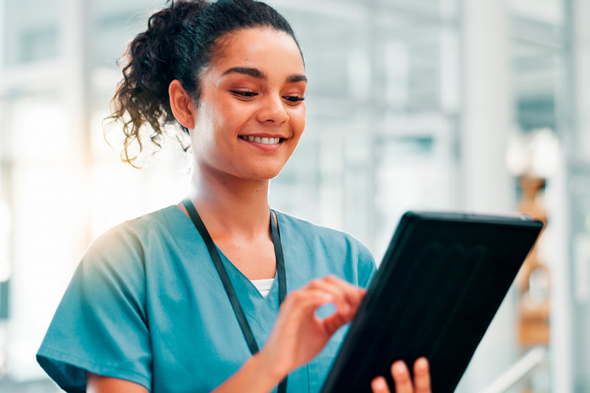 A person in scrubs smiling while reviewing something on a tablet.