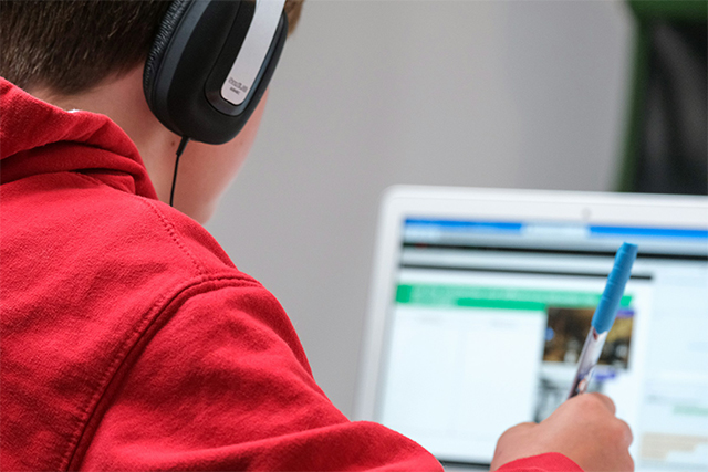 A person wearing headphones and a red shirt as seen from behind as they use a computer.