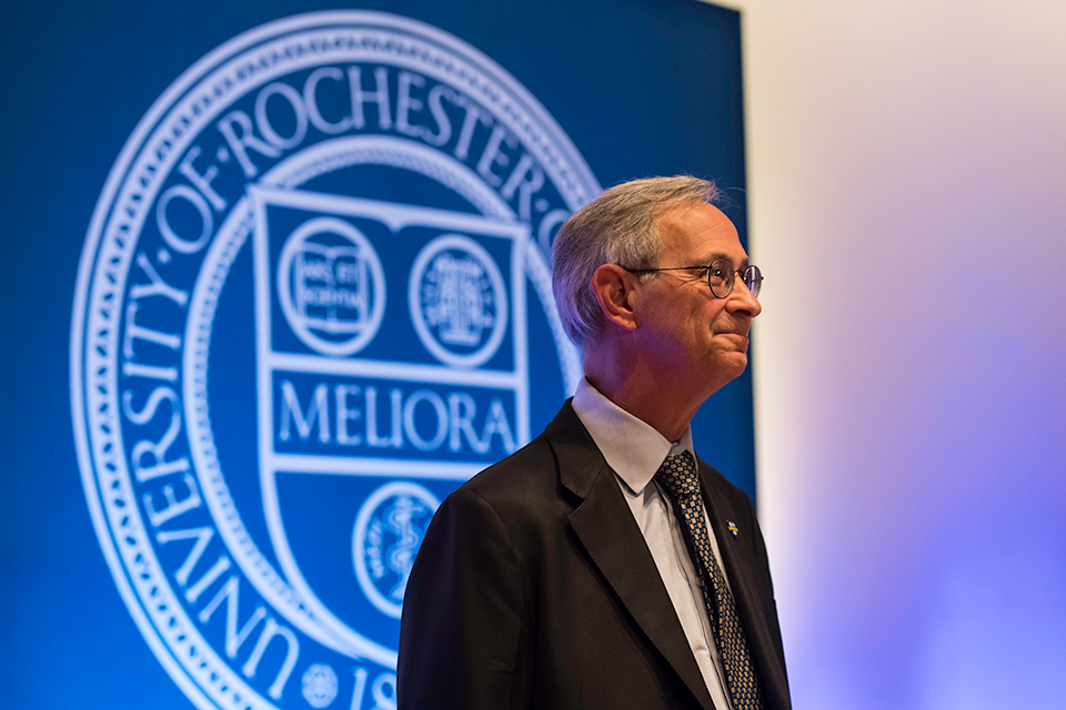 Joel Seligman stands on stage in front of MELIORA shield