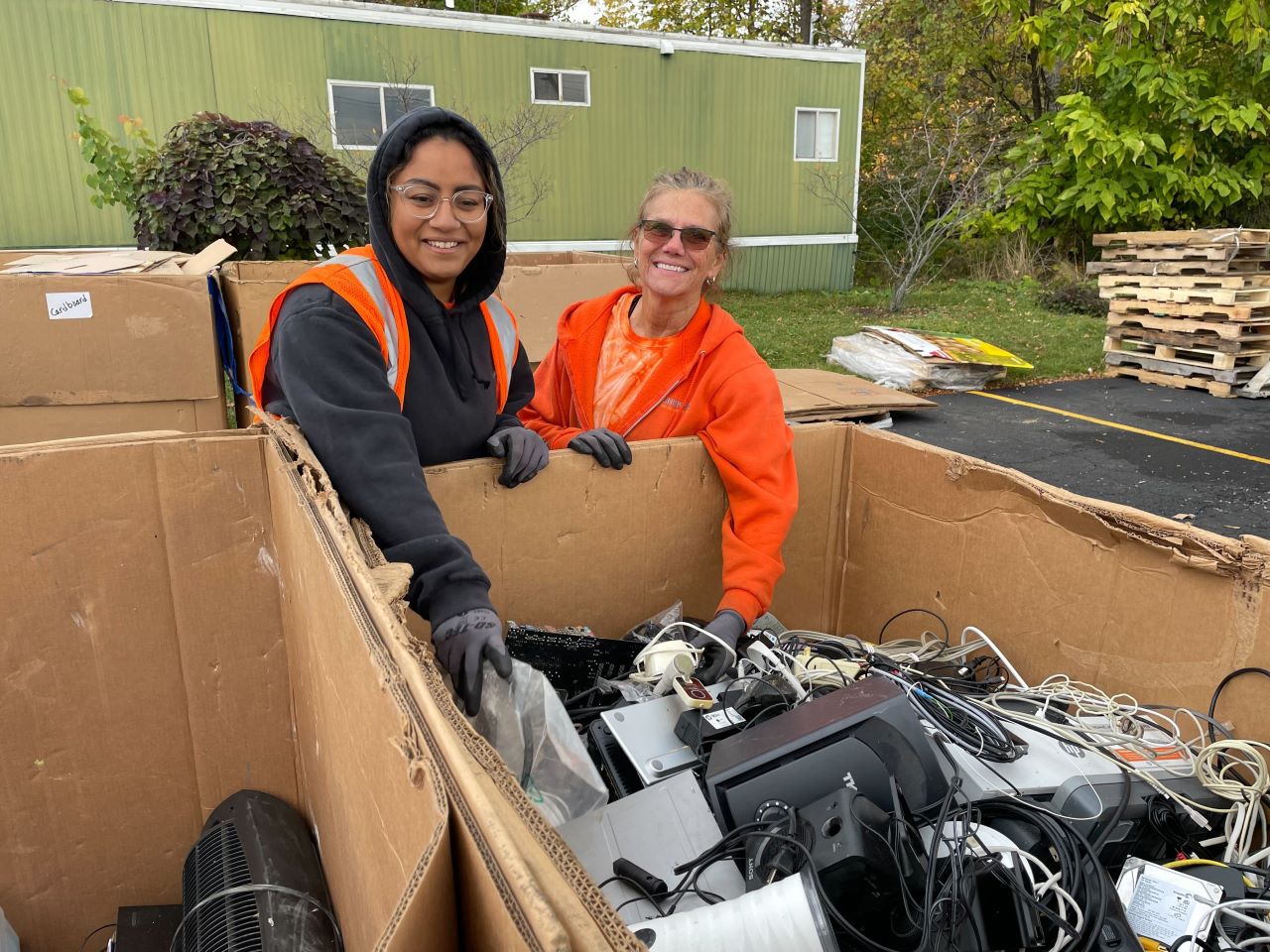 Two University of Rochester volunteers in front of a box filled with recycled electronic devices like monitors, computers, etc.