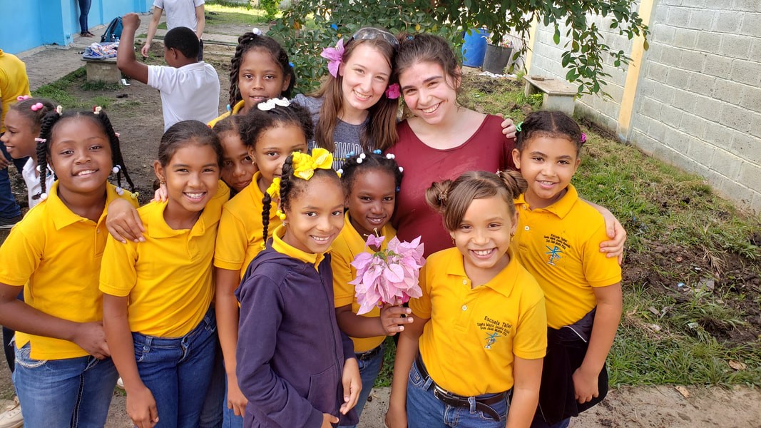 Two University of Rochester student volunteers pictured with a group of primary school kids