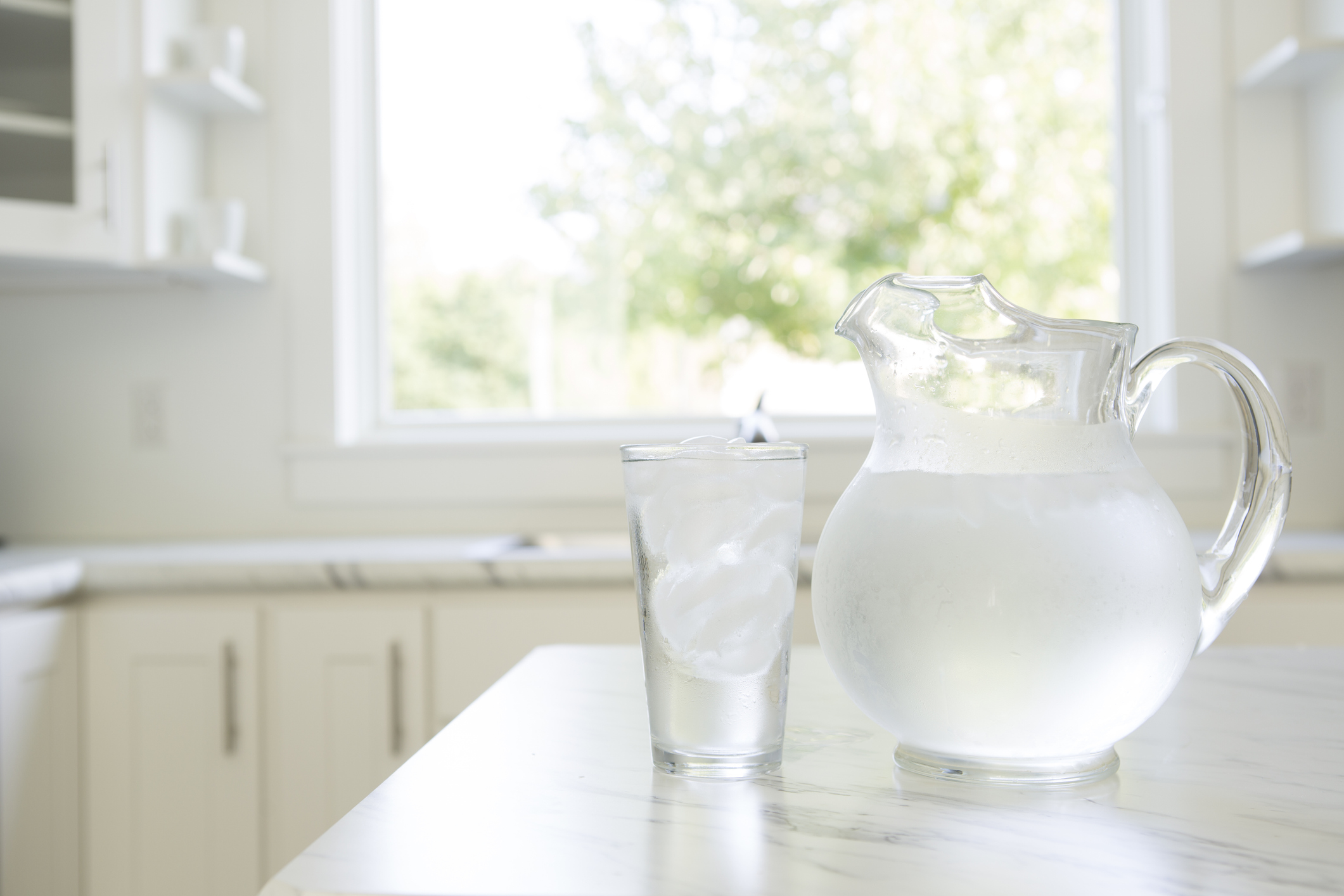 A water pitcher and cold glass of water on a kitchen countertop