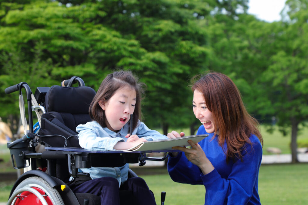 A young girl with muscular dystrophy in a wheelchair drawing a picture, with her mother cheering her on