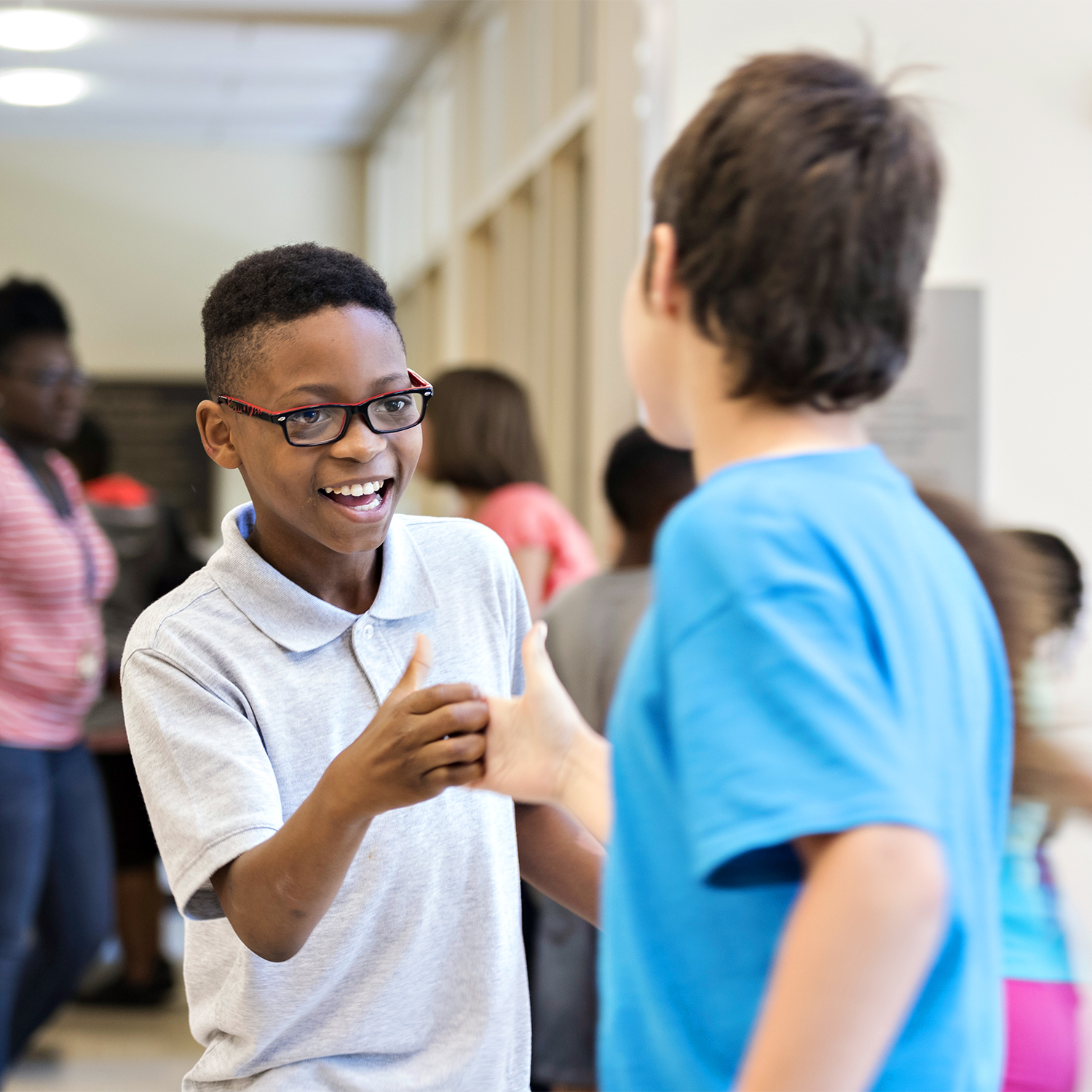 Two young boys shaking hands and smiling in the hallway.