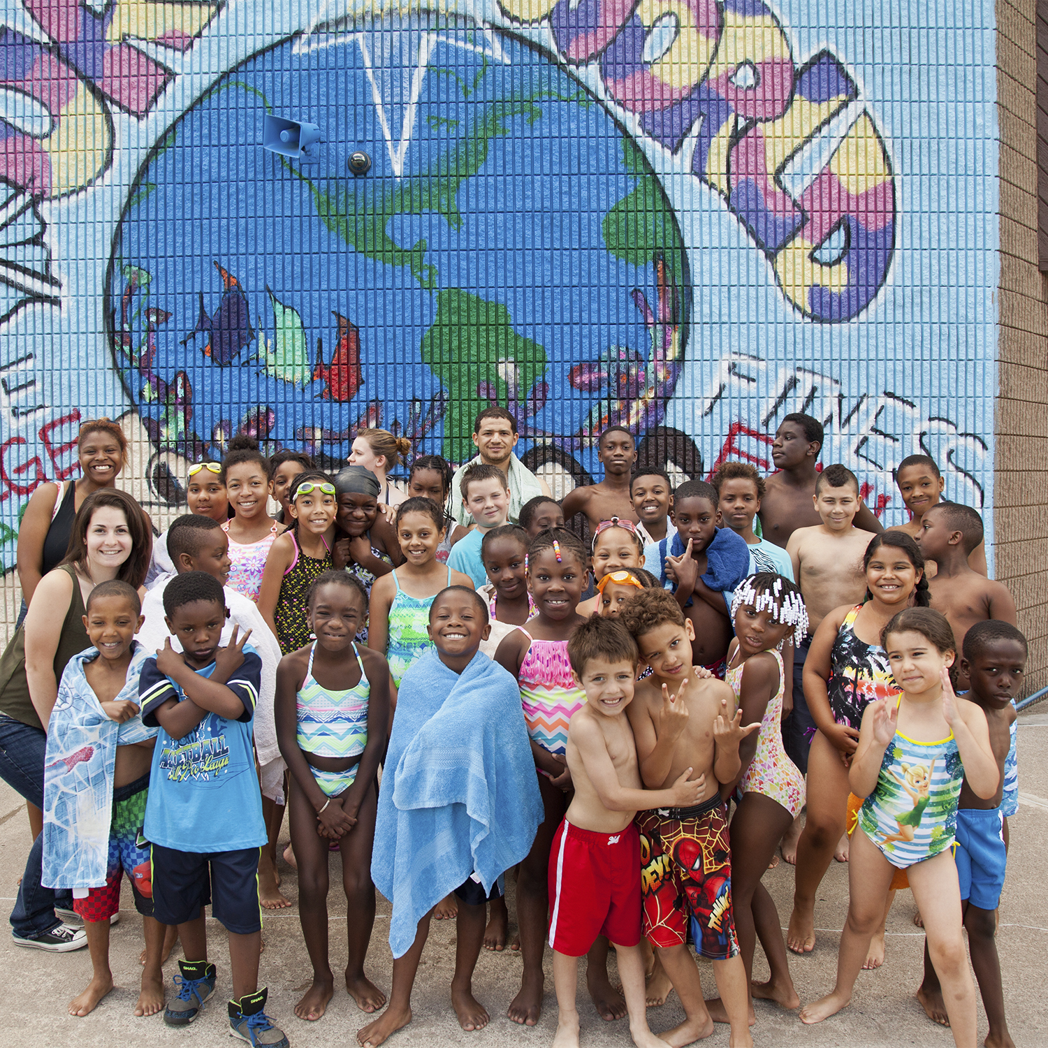 A group of young students in swimsuits posing in front of a mural at the swimming pool.