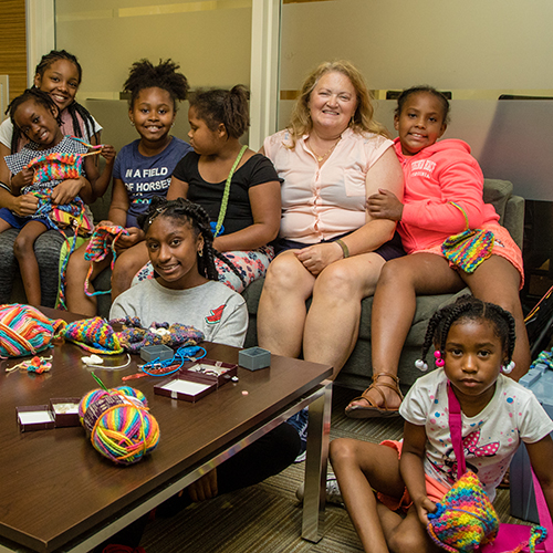 Children gathered around volunteer on a couch who taught them how to crochet