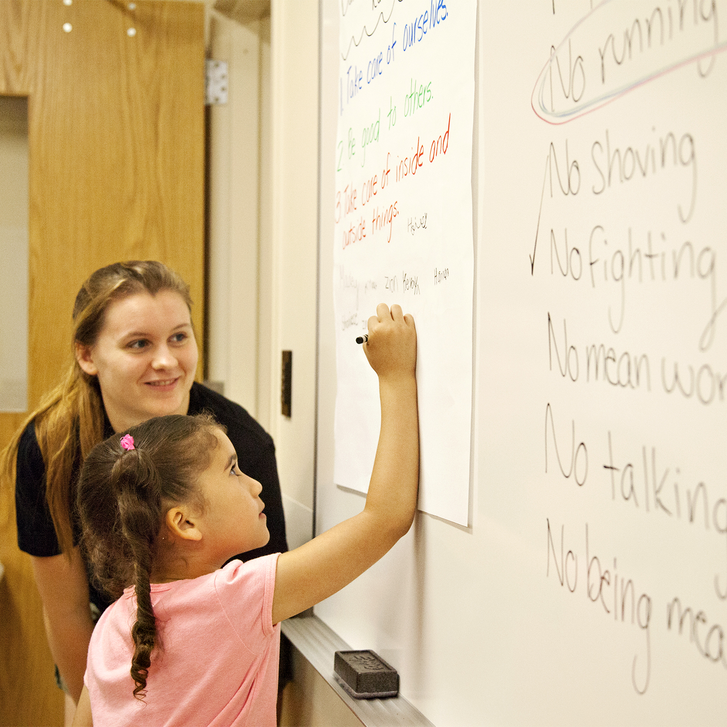 A teacher with a young student writing on the white board.