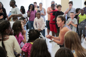 Woman leading a circle of kids in dancing.