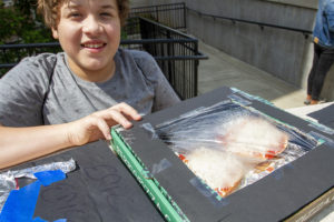 Young student smiling with his pizza box oven, steam can be seen through the plastic wrap.