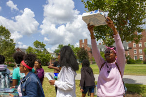 Students outside LeChase hall holding up their pizza box ovens up to the sun.