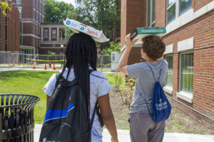 Two students with their solar-pizza box ovens on their heads facing the sun.