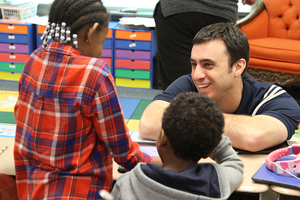 teacher smiling as he interacts with two students