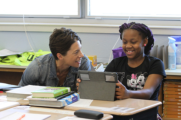 a teacher and student smile while working at an ipad